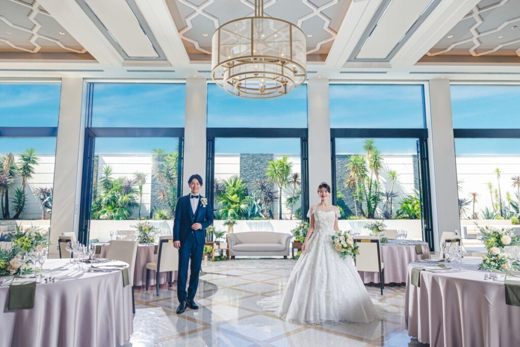 三島の結婚式場ラグシエナの披露宴会場で、新郎新婦が大きな窓から緑が広がる空間に立つウェディングシーン。