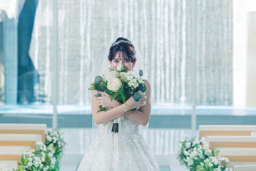 三島の結婚式場ラグシエナのチャペルで、新婦がブーケを持って立つウォーターウォール前のワンシーン。