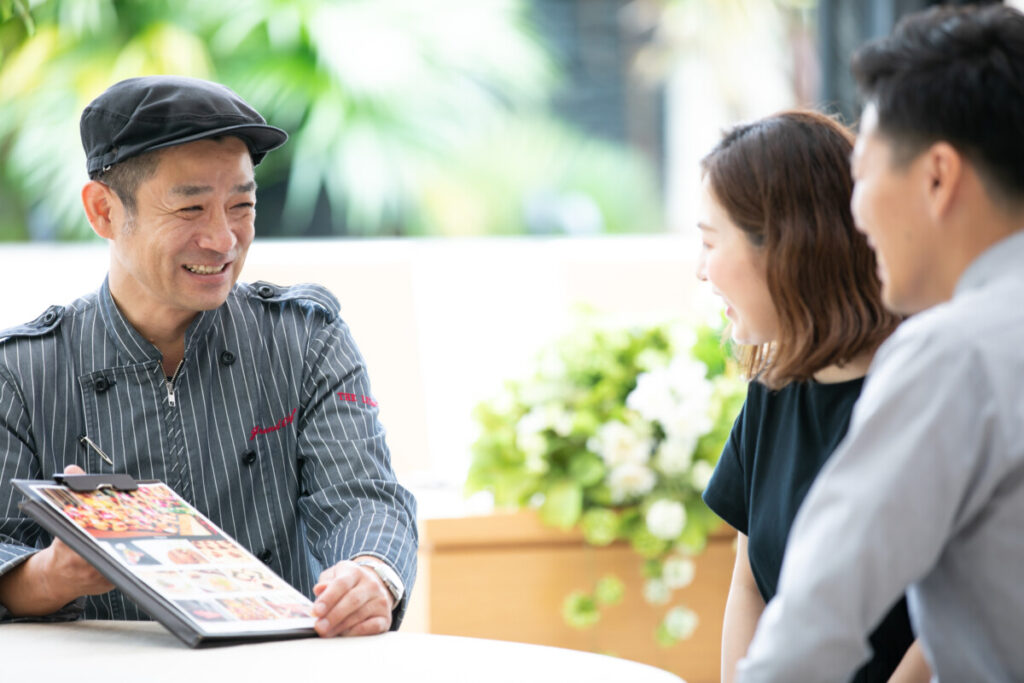 三島の結婚式場ラグシエナで、シェフが新郎新婦に料理メニューを丁寧に提案している相談シーン。