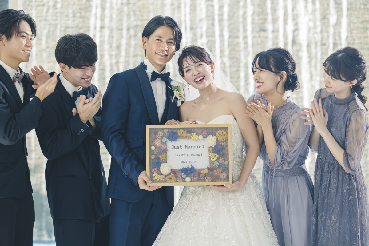三島の結婚式場ラグシエナ。水のカーテンを背景に、新郎新婦とゲストがJust Marriedボードを持って笑顔で並ぶ集合写真。