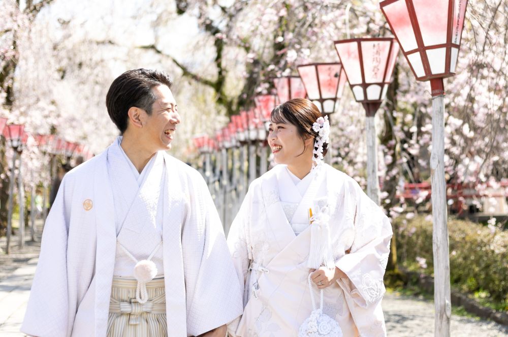 三嶋大社周辺の桜並木を和装姿で歩く新郎新婦。三島・沼津・富士エリアで人気の少人数婚・家族婚の和婚スタイルで、親族中心のアットホームな神前式の様子を表す一枚。