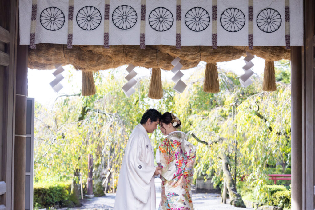 三嶋大社の大きな注連縄の下で撮影した和装の新郎新婦。家族婚・少人数婚の結婚式で人気のロケーションフォトで、白無垢と色打掛が美しく映える一枚。