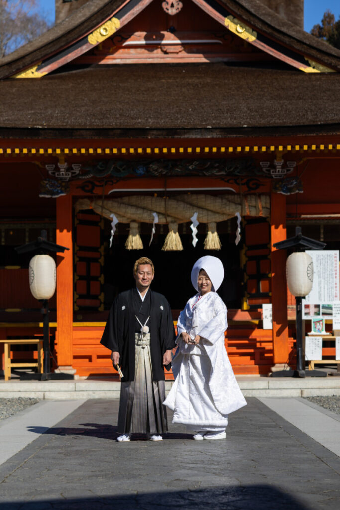 富士山本宮浅間大社の拝殿前で、和装の新郎新婦が並んで立つ神前式の記念写真。