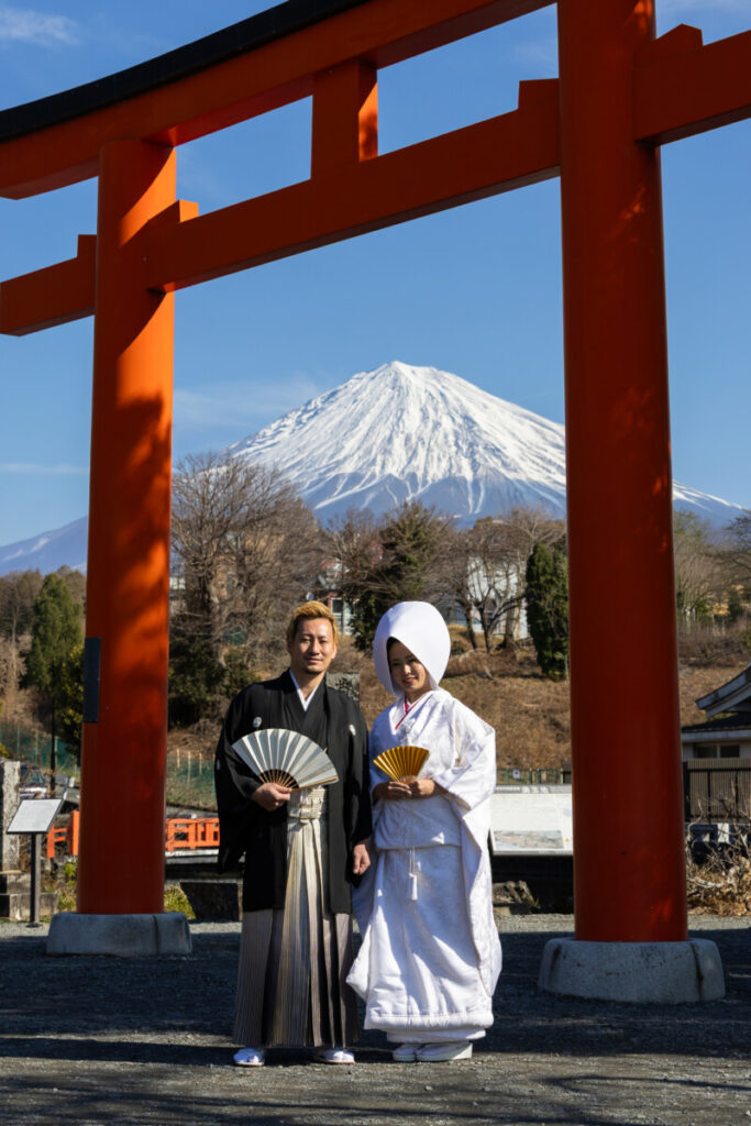 富士山本宮浅間大社の大鳥居の前で和装姿の新郎新婦が並ぶ神前式の写真
