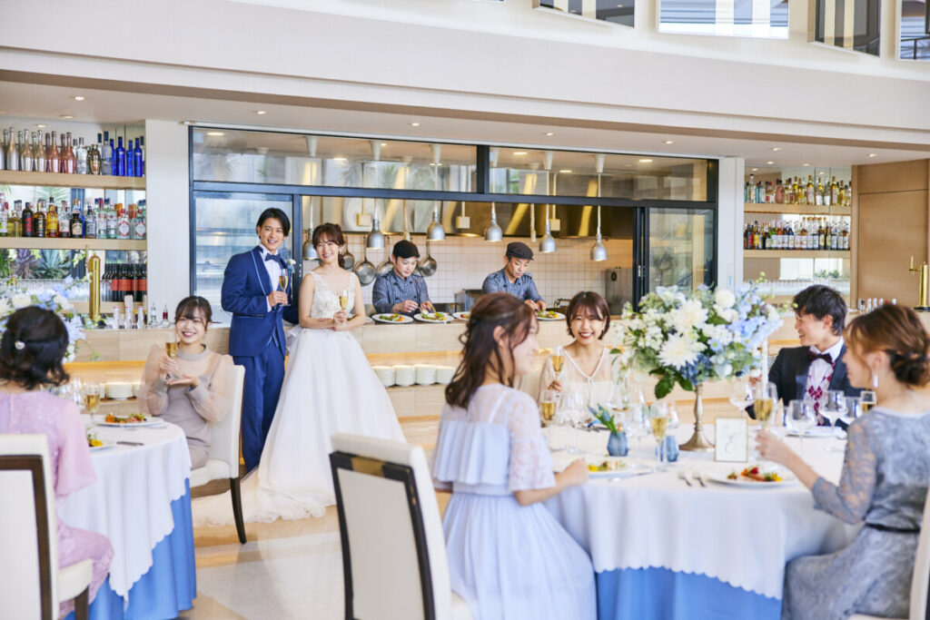 ラグシエナの披露宴で、新郎新婦がゲストと乾杯する様子。オープンキッチンと華やかな会場が印象的なシーン。