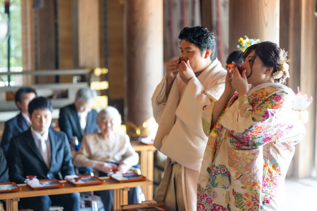 三嶋大社での神前式。色打掛の花嫁と白装束の新郎が三三九度の儀式で盃を交わす様子。
