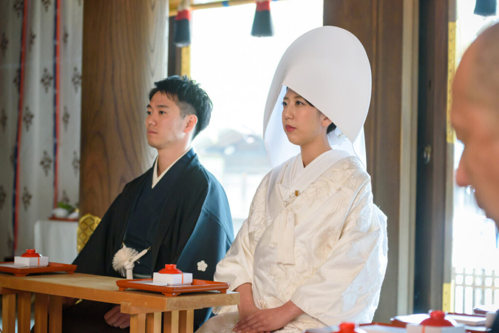 三嶋大社での神前式。白無垢姿の花嫁と黒紋付の新郎が神前に並び、誓いを交わす厳かなシーン。