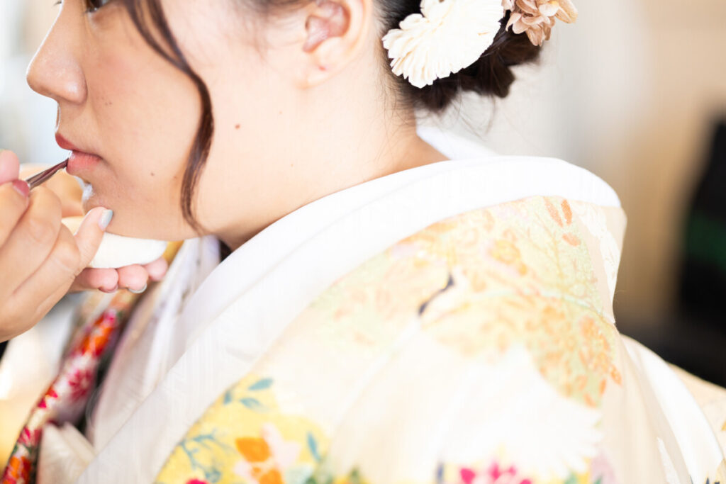 結婚式の支度中、和装の花嫁がリップメイクを受ける美しい準備のひととき。
