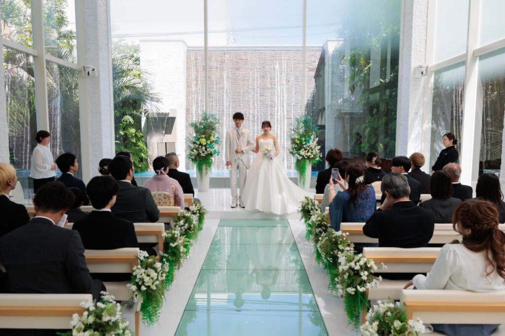 三島・沼津・富士エリアの結婚式場ラグシエナで行われた少人数婚・家族婚のチャペル挙式。ガラスのバージンロードに自然光が差し込み、新郎新婦がゲストに見守られながら誓いを交わすアットホームな家族だけ 結婚式や親族婚にも人気の少人数 結婚式スタイル。