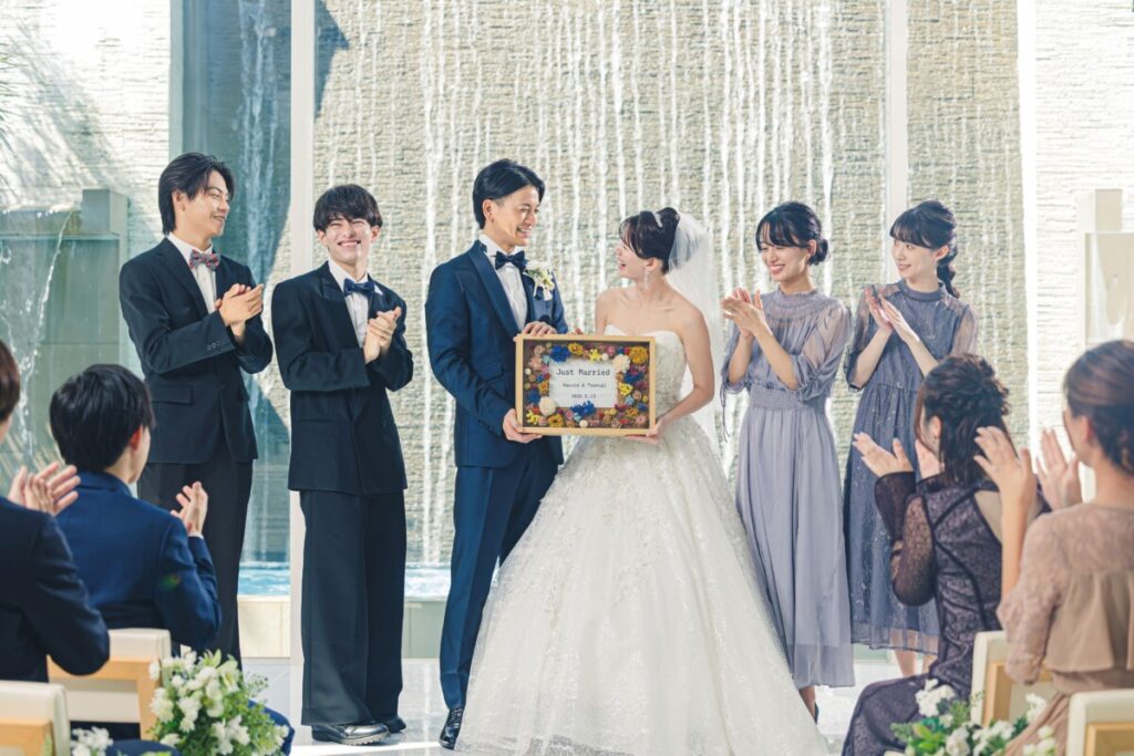 三島の結婚式場ラグシエナで行われた少人数婚・家族婚のアフターセレモニー。新郎新婦NaotoとTomomiが「Just Married」ボードを掲げ、ゲストに祝福される記念写真。三嶋大社の神前式と会食婚に対応した少人数 結婚式の実例。